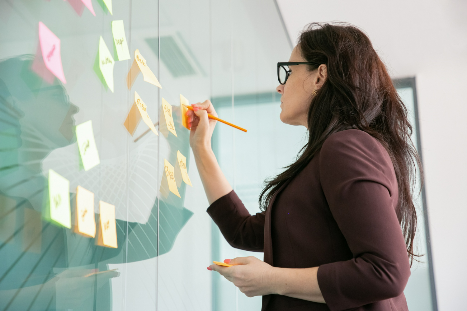 confident middle aged businesswoman writing on sticker with pencil and brainstorming