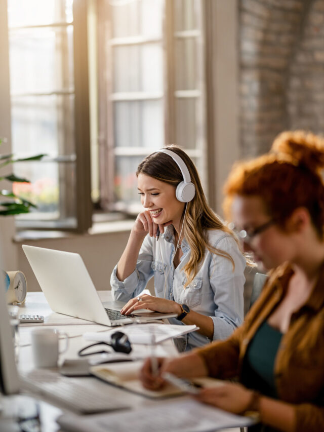 Happy businesswoman with headphones working on laptop in the off