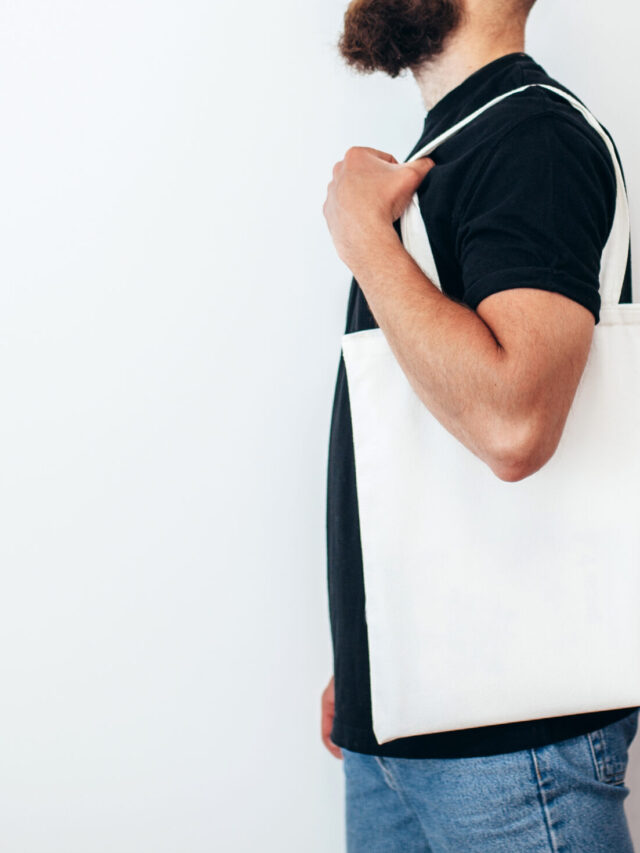 Young man is holding white textile eco bag on white background. Mockup for design