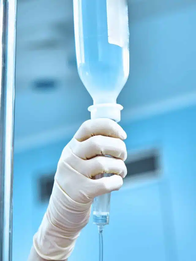 Dropper into a vein close-up on a background of the surgical operational. Doctor woman in sterile gloves preparing a patient for surgery.