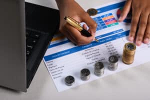 uma pessoa preenchendo uma lista de verificacao com moedas e um laptop moeda brasileira