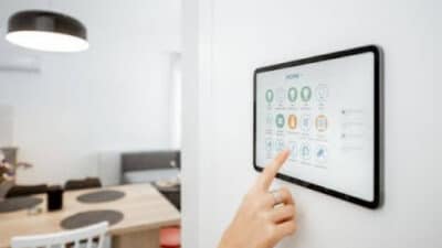 Pessoa utilizando painel touchscreen de automação residencial instalado na parede para controlar funções inteligentes da casa.