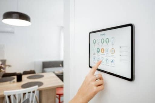 Pessoa utilizando painel touchscreen de automação residencial instalado na parede para controlar funções inteligentes da casa.