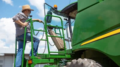 professional farmer with modern tractor work process looks confident bright summer colors sunshine agriculture exhibition machinery plant production senior man s climbing machine
