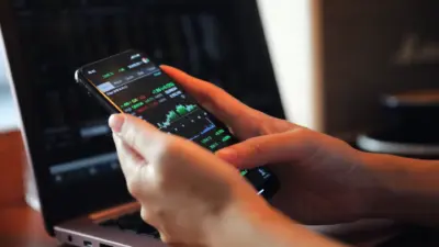 mao segurando smartphone com graficos mercado financeiro