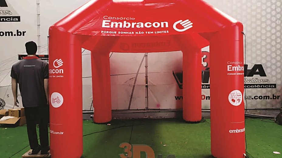 Montagem de tenda para evento: etapas e segurança 2 Tenda inflável vermelha de quatro pernas com marca impressa no teto e nas pernas, montada dentro de um galpão