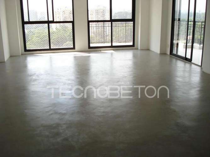 Piso de cimento queimado: como é feito e o que pedir 3 Sala vazia com piso de cimento queimado cinza contínuo refletindo a luz de janelas amplas