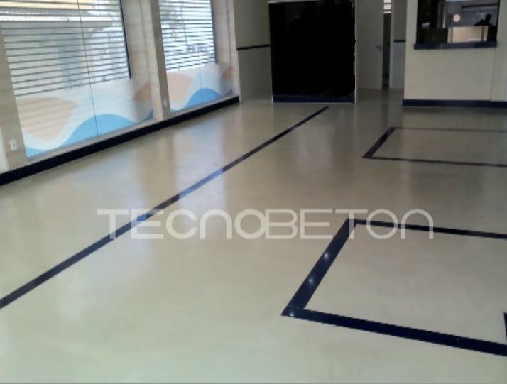 Porcelanato cimento queimado ou cimento queimado? 2 Piso cimentício claro e contínuo em área comercial, com faixas escuras decorativas e janelas ao fundo
