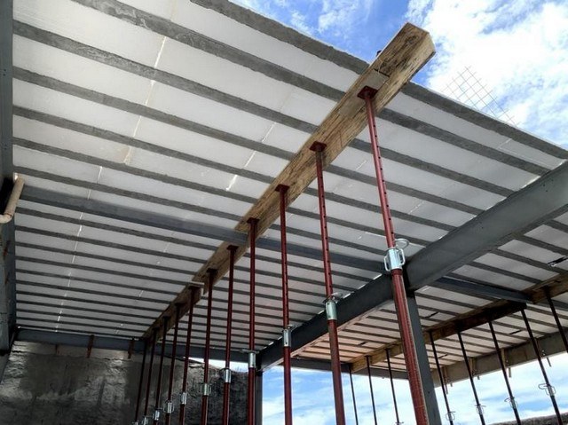 Laje de isopor é segura? Carga, construir em cima e fogo 2 Face inferior de uma laje com blocos brancos de EPS, sustentada por escoras metálicas vermelhas e uma viga de madeira