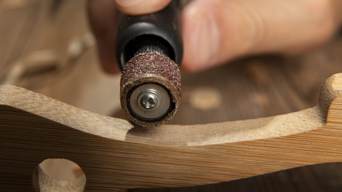 Acessórios para micro retífica: qual usar em cada material 3 Micro retífica com cilindro de lixa marrom lixando a borda curva de uma peça de madeira