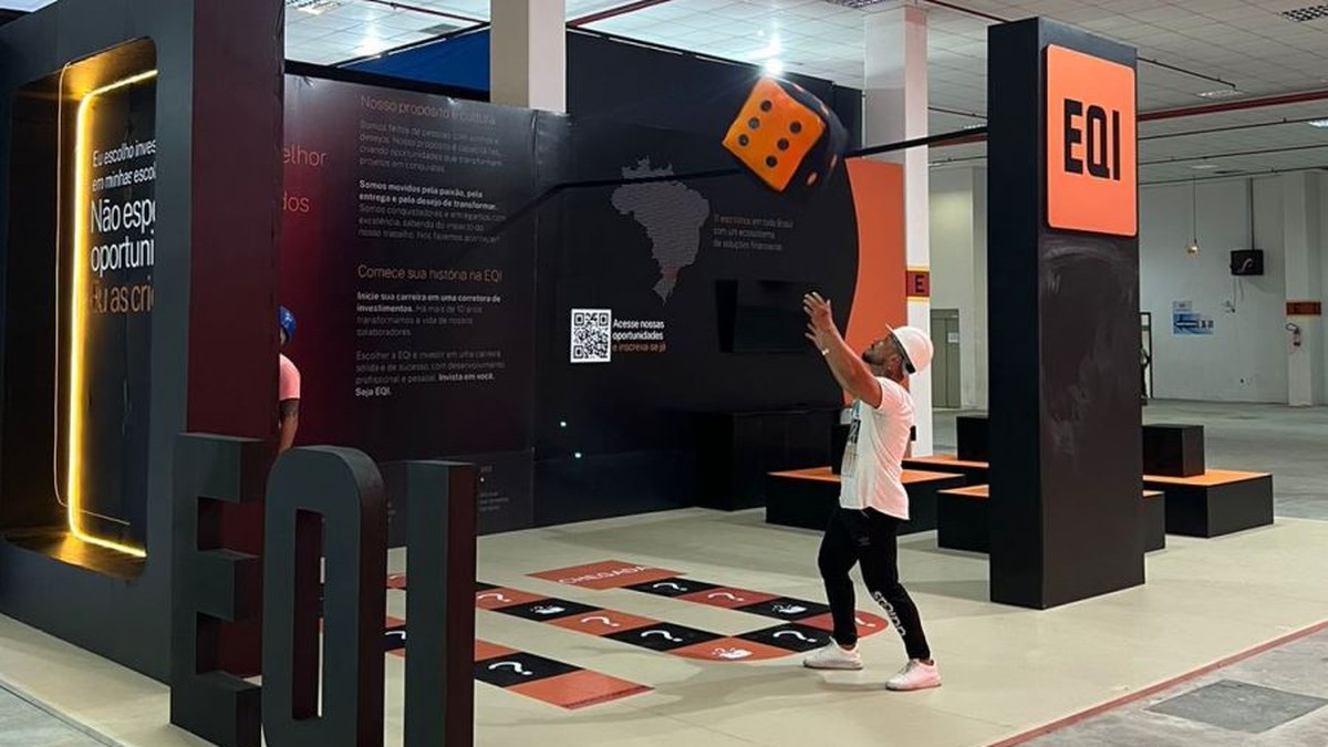 O que é cenografia: como funciona em eventos e stands 2 Stand cenográfico preto e laranja com letras tridimensionais da marca, dado gigante suspenso e jogo de amarelinha pintado no piso