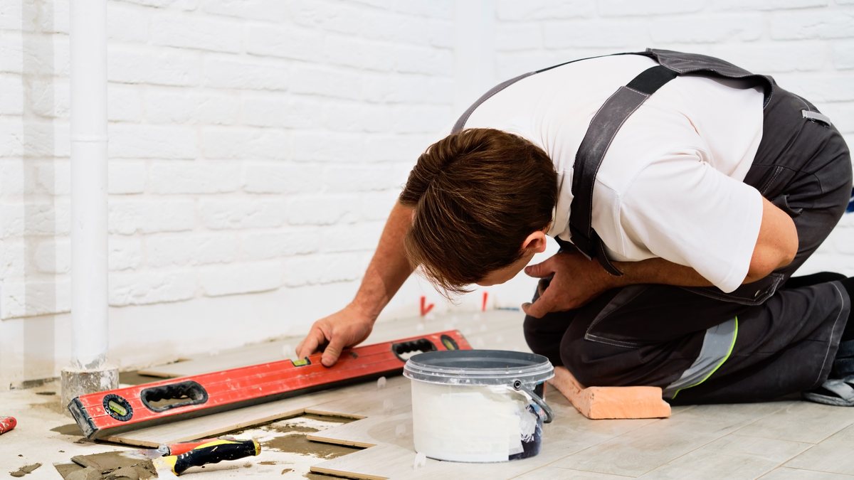 Diferença entre porcelanato e cerâmica: como escolher 2 Assentador confere com nível de bolha o alinhamento de placas cerâmicas recém-assentadas no piso