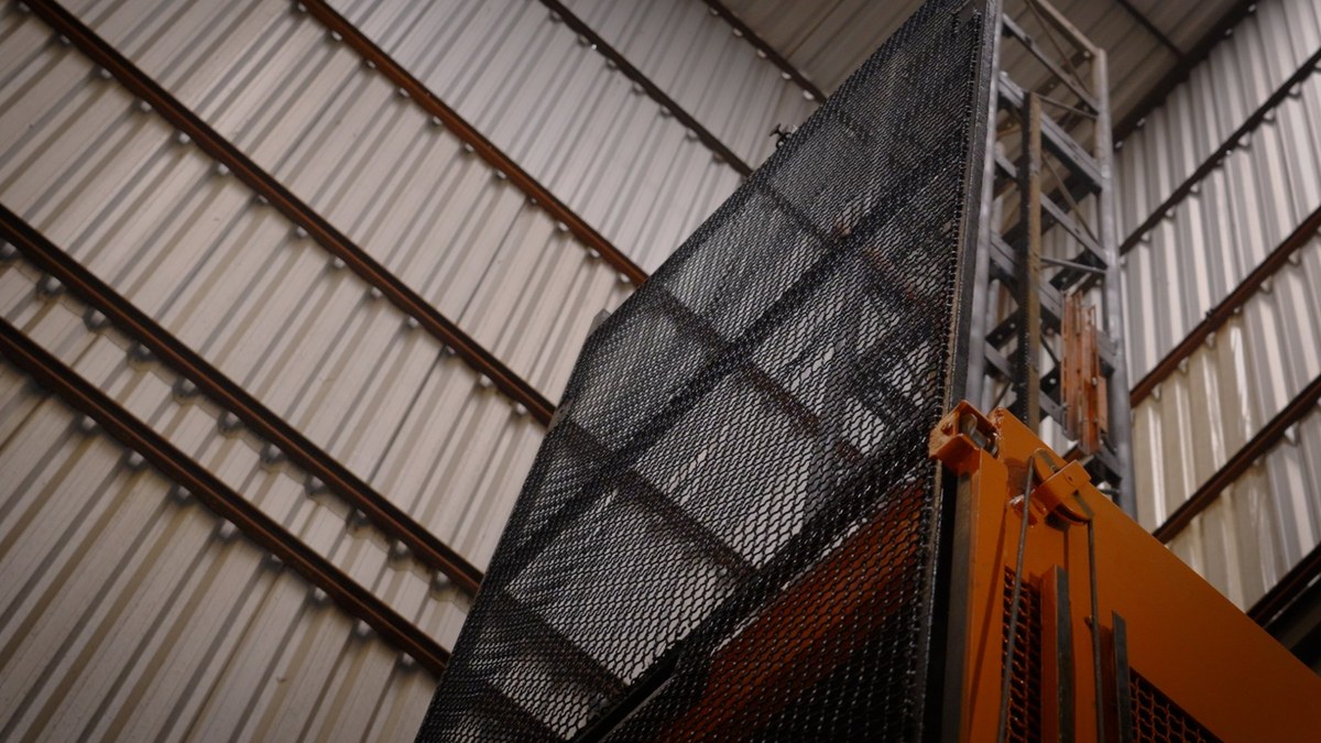 Operador de elevador cremalheira: quem pode operar 2 Detalhe da porta de grade metálica e da torre de uma cabina de elevador cremalheira laranja sob cobertura metálica