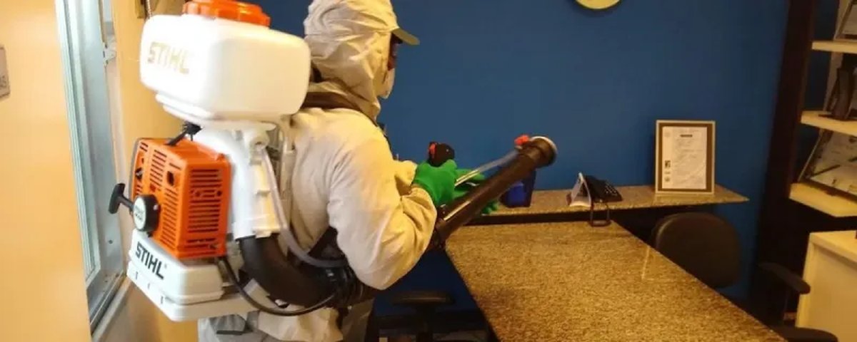Terceirização de limpeza hospitalar: o que exigir 2 Agente da RIAN Facilities com equipamento de proteção e atomizador costal desinfetando um escritório