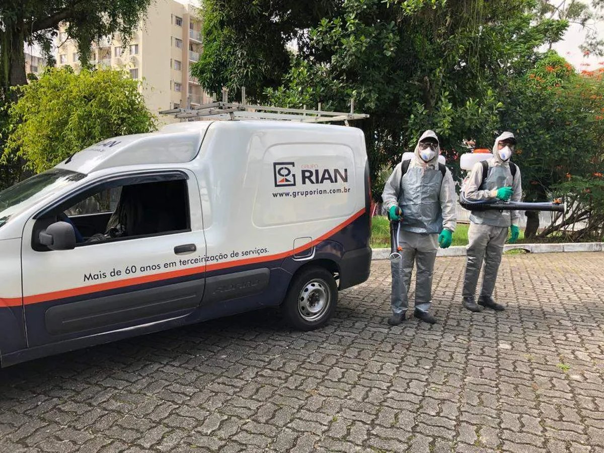 Limpeza industrial terceirizada: escopo, riscos e contrato 2 Van branca com a marca Grupo Rian e dois agentes com macacão, máscara, luvas e pulverizador costal