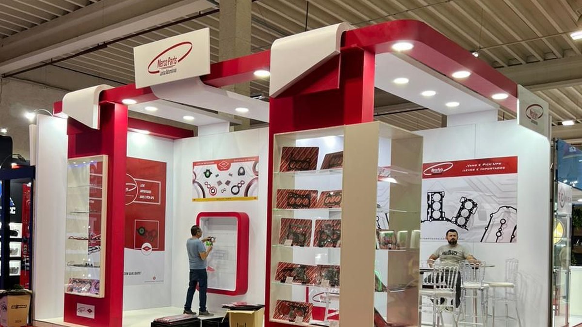 Stand ou estande: o que é e para que serve na feira 3 Stand construído branco e vermelho, com pórticos de marcenaria, prateleiras iluminadas com produtos e mesa alta com banquetas