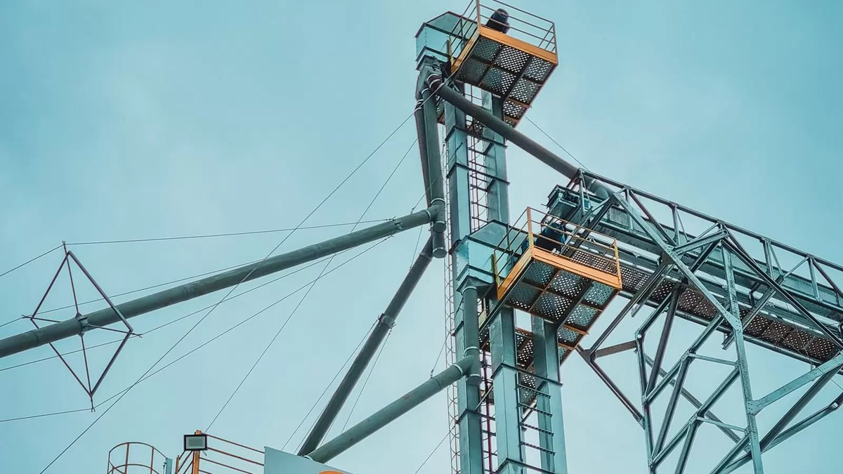 Secador intermitente ou contínuo: diferenças e como escolher 2 Parte superior de torre de secador de grãos metálica, com escada externa, plataforma e dutos de ligação ao elevador