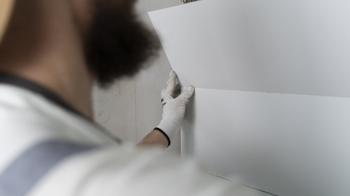 Tipos de revestimento: como escolher para cada ambiente 2 Assentador posiciona placa cerâmica branca de grande formato em parede de apartamento em reforma