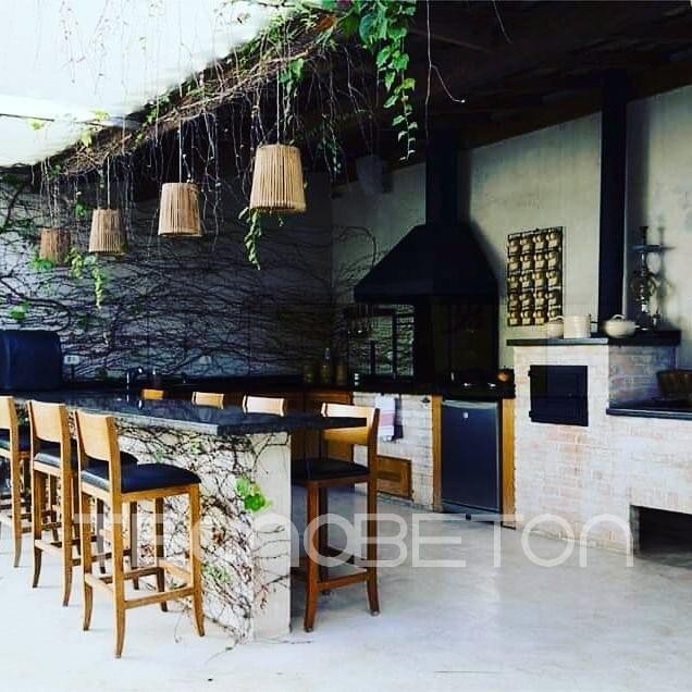 Tipos de revestimento: como escolher para cada ambiente 3 Área gourmet externa com bancada e paredes em acabamento cimentício cinza, banquetas de madeira e luminárias de palha